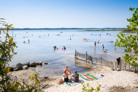 Famiglie si rilassano e nuotano nel lago al Huttopia Lac de Carcans in Nouvelle-Aquitaine, Francia.