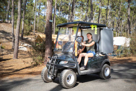 Dos jóvenes conducen un carrito de golf en el camping arbolado del parque vacacional Huttopia Lac de Carcans, Francia.