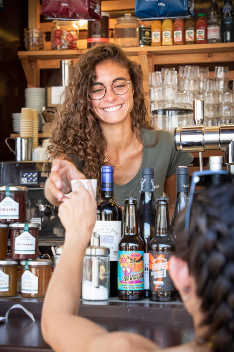 Lächelnde Barista serviert Kaffee an der Theke im Ferienpark Huttopia Lac de Carcans, Frankreich.