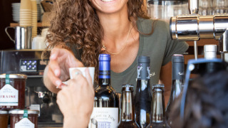 Lächelnde Barista serviert Kaffee an der Theke im Ferienpark Huttopia Lac de Carcans, Frankreich.