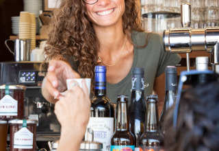 Barista sonriente sirviendo café a un huésped en Huttopia Lac de Carcans, Nueva Aquitania, Francia.