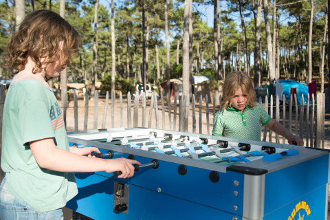 Dos niños jugando futbolín al aire libre bajo el sol en Huttopia Lac de Carcans, parque vacacional en Francia.
