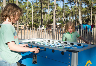 Zwei Kinder spielen Tischfußball im Freien bei Sonnenschein im Huttopia Lac de Carcans Ferienpark, Frankreich.