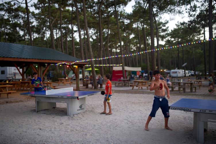 Kinder spielen Tischtennis unter Lichterketten im Ferienpark Huttopia Lac de Carcans in Frankreich.