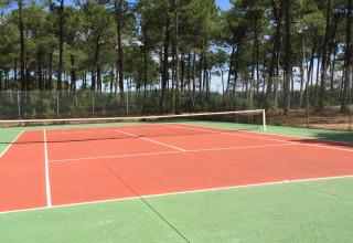 Udendørs tennisbane ved Huttopia Lac de Carcans, omgivet af fyrretræer og blå himmel i Nouvelle-Aquitaine.