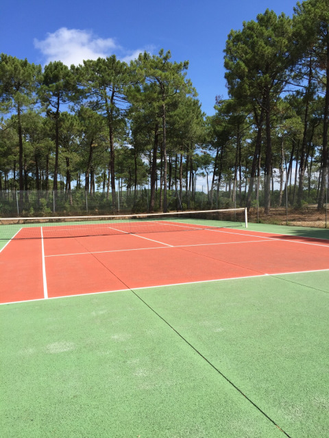 Udendørs tennisbane ved Huttopia Lac de Carcans, omgivet af fyrretræer og blå himmel i Nouvelle-Aquitaine.