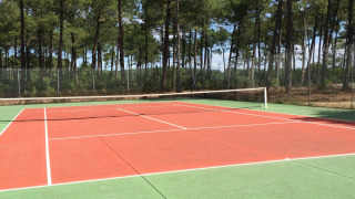 Tennisplatz im Freien im Ferienpark Huttopia Lac de Carcans, umgeben von Bäumen, in Nouvelle-Aquitaine.