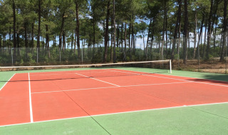 Tennisplatz im Freien im Ferienpark Huttopia Lac de Carcans, umgeben von Bäumen, in Nouvelle-Aquitaine.