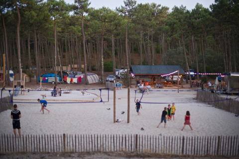 Niños y adultos juegan al voleibol en la arena en Huttopia Lac de Carcans, rodeados de bosque y tiendas.