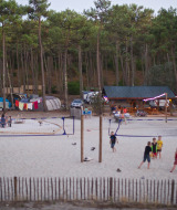 Kinder und Erwachsene spielen Volleyball im Sand in Huttopia Lac de Carcans, umgeben von Wald und Zelten.