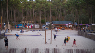 Kinder und Erwachsene spielen Volleyball im Sand in Huttopia Lac de Carcans, umgeben von Wald und Zelten.