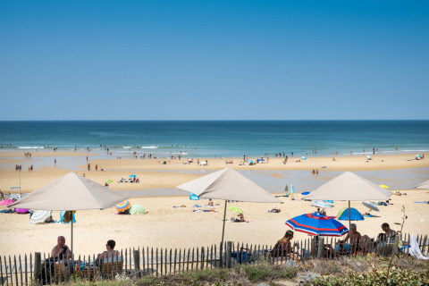 Playa soleada en Huttopia Lac de Carcans en Nouvelle-Aquitaine, Francia, con sombrillas y gente disfrutando.