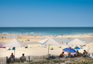 Sommerdag på stranden ved Huttopia Lac de Carcans, folk nyder solen under parasoller, Nouvelle-Aquitaine, Frankrig.