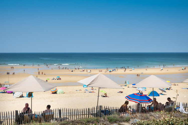 Sunny beach scene at Huttopia Lac de Carcans, Nouvelle-Aquitaine, France, with parasols and people relaxing.
