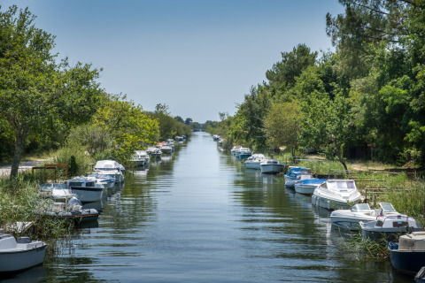 Boats moored along a peaceful canal at Huttopia Lac de Carcans holiday park, Nouvelle-Aquitaine, France.