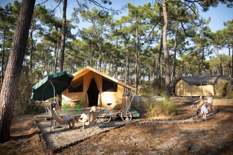 Safari tent Toile&bois Classic bij Huttopia Lac de Carcans in Frankrijk, omgeven door dennen en fietsen.