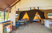 Interior view of a safari tent featuring wooden floor, dining area, small kitchen, and bunk beds in back.
