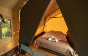 Intérieur d'une tente safari avec un lit double et deux chaises, baigné par la lumière naturelle.