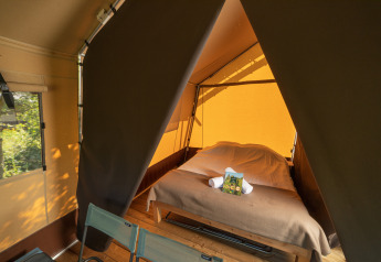 Interieur van een safaritent met een tweepersoonsbed, twee stoelen en zonlicht door het tentdoek.