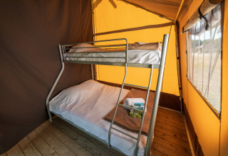 Intérieur d'une tente safari avec un lit superposé et un plancher en bois, parfait pour un séjour confortable.
