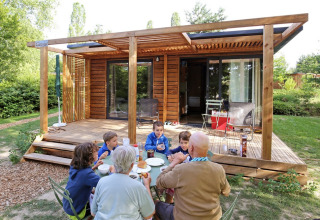 Family shares breakfast outdoors in front of a wooden cabin at Huttopia Etang de Fouché, Burgundy, France.