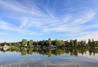 Refleksion af grønne træer og blå himmel i søen ved Huttopia Etang de Fouché, Bourgogne-Franche-Comté, Frankrig.