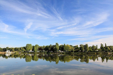 Riflessione degli alberi verdi e del cielo blu sul lago a Huttopia Etang de Fouché, Bourgogne-Franche-Comté, Francia.