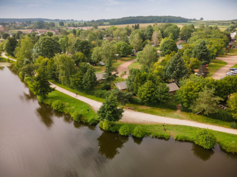 Vue aérienne d’un parc de vacances avec cabanes, sentiers et verdure au bord d’un étang en Bourgogne.