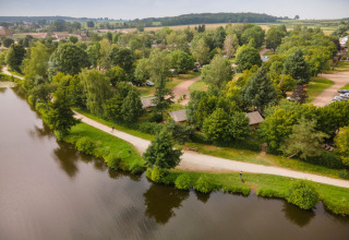 Aerial view of a holiday park with cabins, pathways, and lush trees by a calm lake in Burgundy, France.