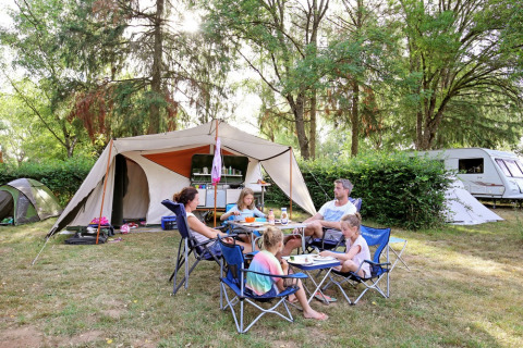 Una familia disfruta de una comida al aire libre frente a una tienda en Huttopia Etang de Fouché en Francia.
