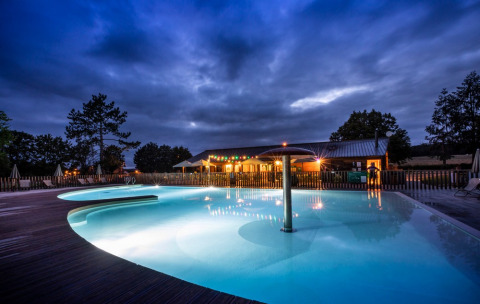 Piscina iluminada en Huttopia Etang de Fouché, un complejo vacacional en Bourgogne-Franche-Comté, Francia, al anochecer.