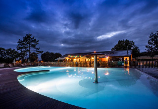 Illuminated swimming pool at Huttopia Etang de Fouché holiday park in Bourgogne-Franche-Comté, France at dusk.