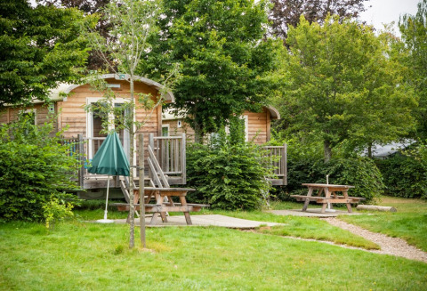 Cabañas de madera entre árboles y mesas de picnic en Huttopia Etang de Fouché, parque vacacional en Borgoña, Francia.