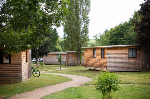 Wooden cabins among trees at Huttopia Etang de Fouché holiday park in Bourgogne, France, with winding paths.