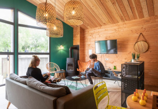Two people relax in a cozy, modern wood cabin living area at Huttopia Etang de Fouché holiday park in France.