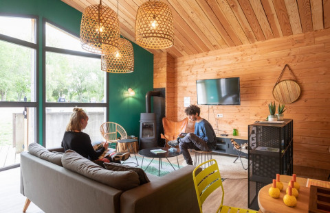Two people relax in a cozy, modern wood cabin living area at Huttopia Etang de Fouché holiday park in France.