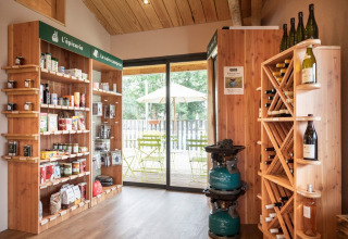 Kleiner Laden im Huttopia Etang de Fouché mit Holzregalen, Lebensmitteln, Wein und Campingzubehör.