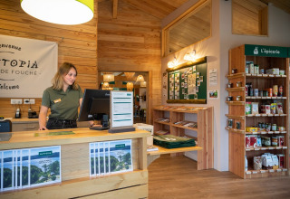 Receptionen på Huttopia Etang de Fouché feriested i Bourgogne, Frankrig, med personale og butikshylder.
