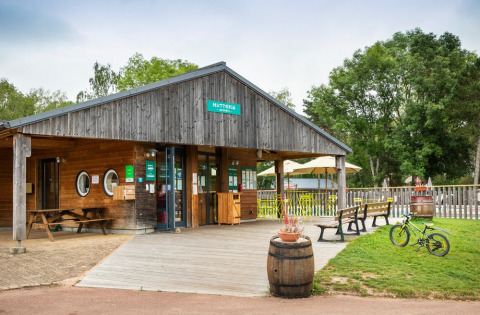 Entrada al parque vacacional Huttopia Etang de Fouché en Bourgogne-Franche-Comté, Francia, con bancos y bicicleta.