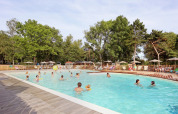 Folk nyder en udendørs swimmingpool omgivet af træer og liggestole i ferieparken Huttopia Etang de Fouché, Frankrig.