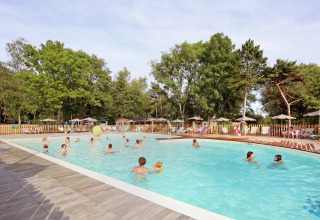 Folk nyder en udendørs swimmingpool omgivet af træer og liggestole i ferieparken Huttopia Etang de Fouché, Frankrig.