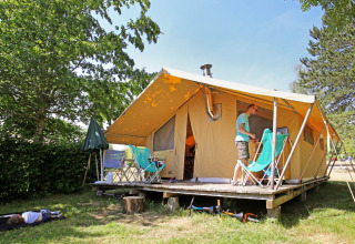 Familie nyder camping udenfor et stort safaritelte med træterrasse i grønne omgivelser ved Huttopia Etang de Fouché.