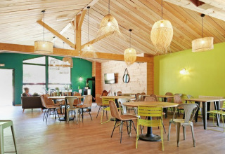 Bright, modern lounge and dining area with wood beams at Huttopia Etang de Fouché holiday park in Burgundy.