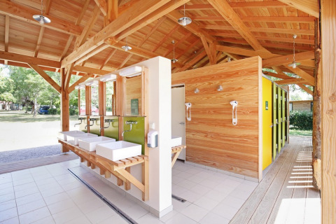 Modernes Gemeinschaftsbad mit Holzbau und gelben Türen bei Huttopia Etang de Fouché, Frankreich.