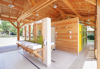 Modernes Gemeinschaftsbad mit Holzbau und gelben Türen bei Huttopia Etang de Fouché, Frankreich.