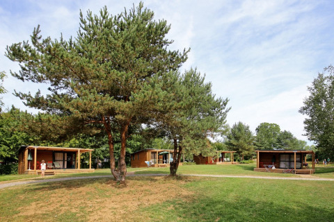 Cabañas de madera en el parque vacacional Huttopia Etang de Fouché rodeadas de árboles y césped en Borgoña, Francia.