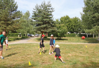 Kinderen en een volwassene spelen een balspel buiten in Huttopia Etang de Fouché vakantiepark in Bourgondië, Frankrijk.