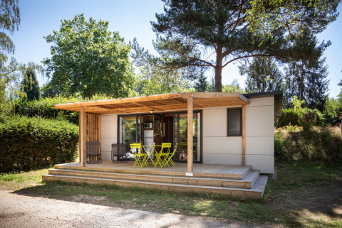 Mobile home Vancouver: Cabaña moderna de madera con terraza cubierta, sillas amarillas, rodeada de árboles.