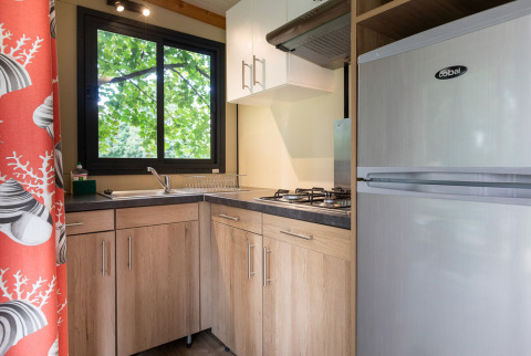 Cocina moderna en Mobile home Vancouver con gabinetes de madera, estufa de gas y ventana a árboles.