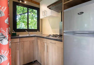 Moderne Küche im Mobile Home Vancouver mit Holzschränken, Gasherd und Fenster mit Baum-Ausblick.
